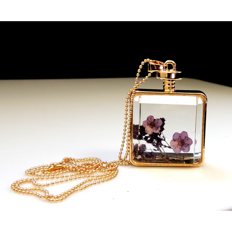 Collier long avec une chaîne perlée dorée qui supporte un flacon en verre contenant des fleurs séchées